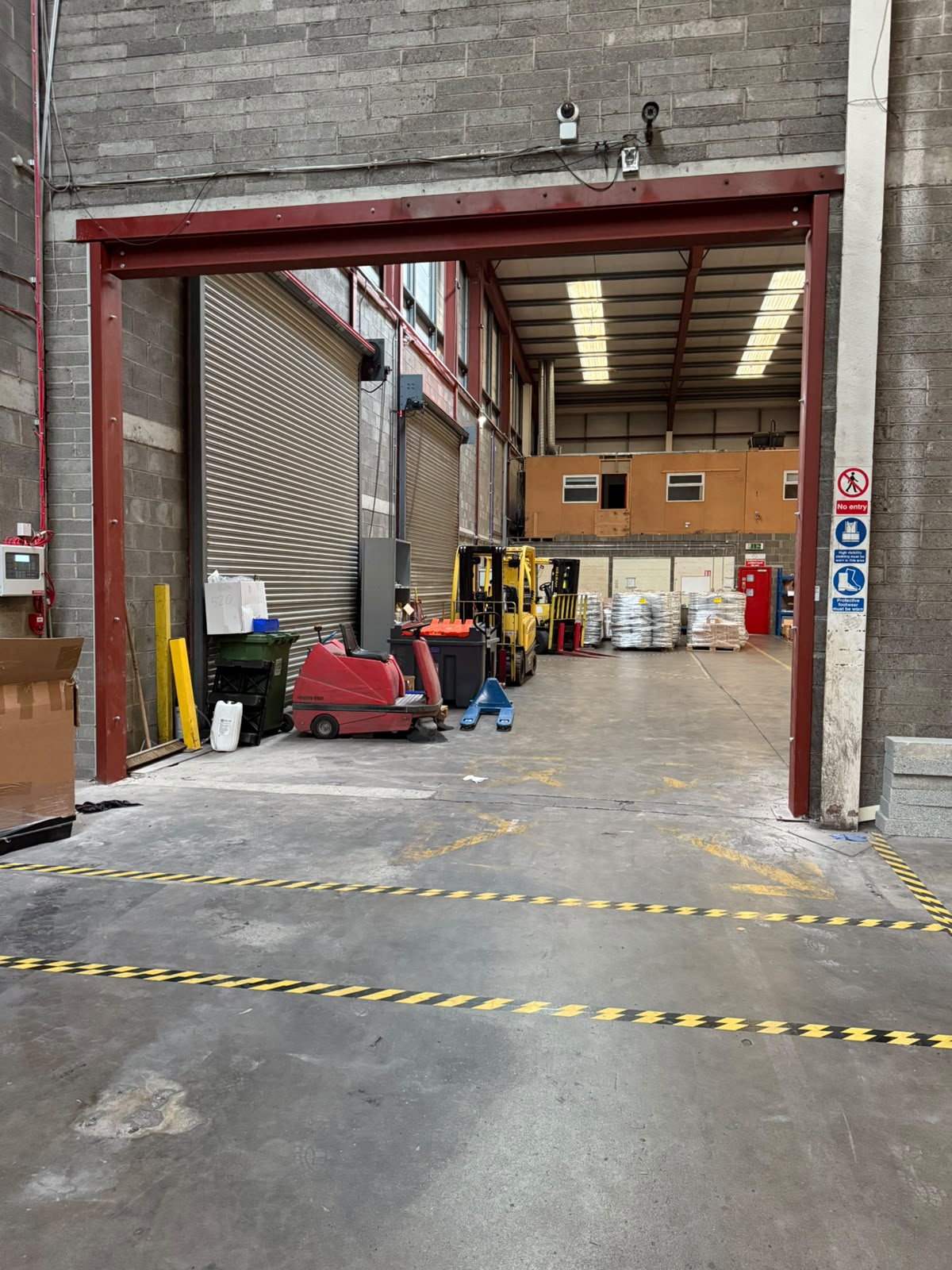 Completed red steel goal post opening through a blockwork wall into a working warehouse