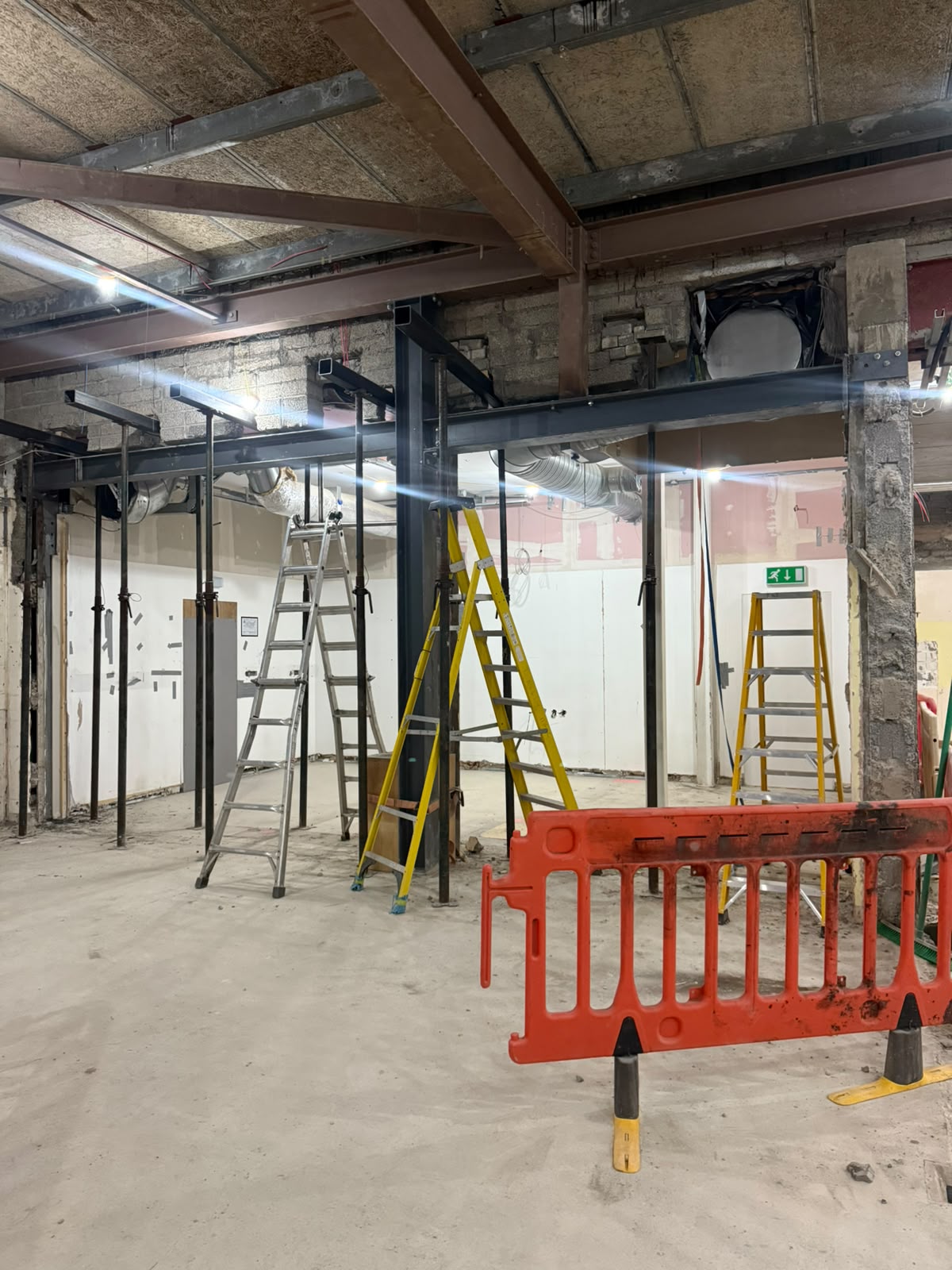New dark grey steel beams and columns on props carrying a wall opening in a stripped out basement fit out