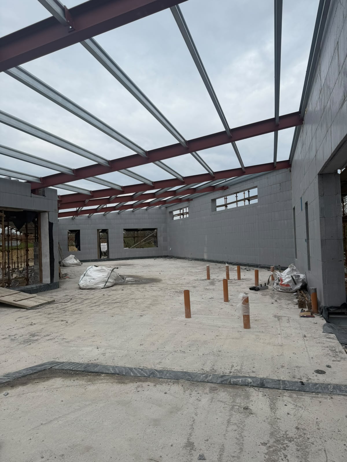 Red oxide roof beams with galvanised purlins spanning across new blockwork walls on a house under construction