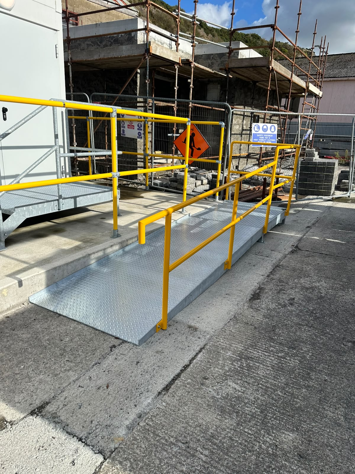 Safety yellow painted steel access ramp and handrails at an industrial building