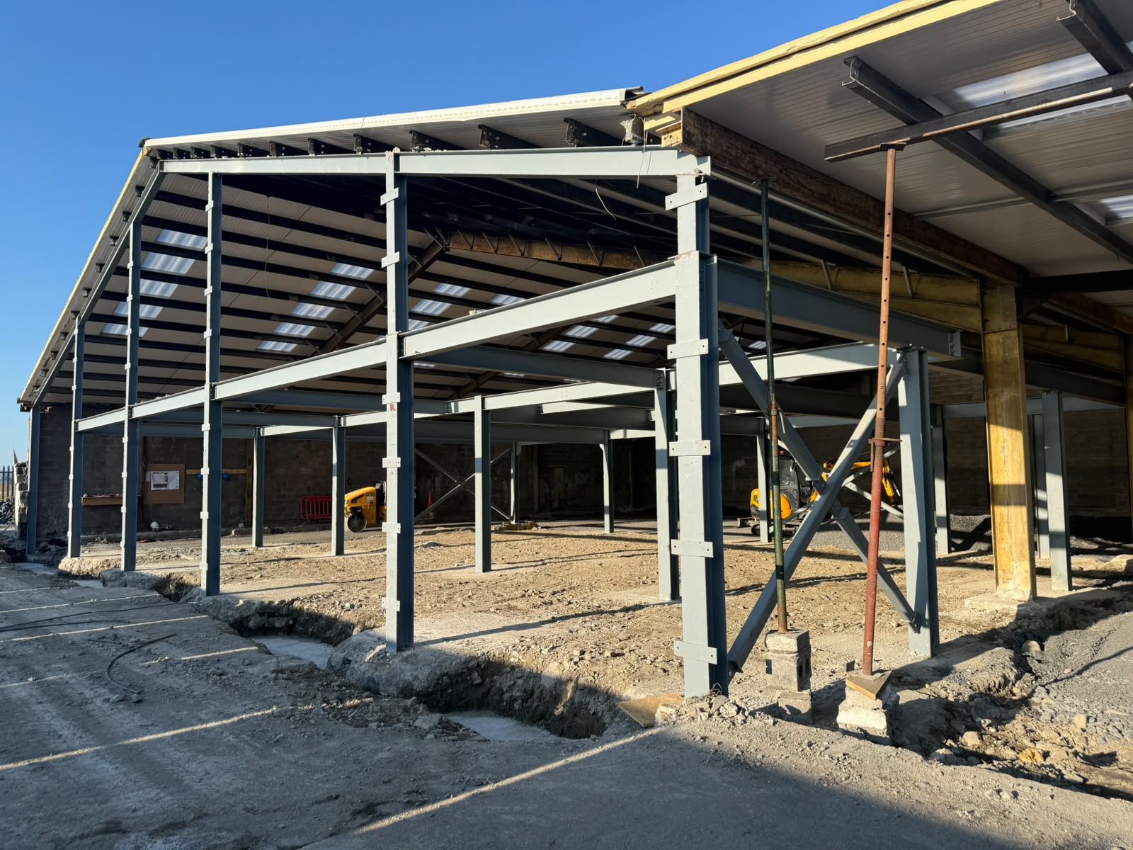 Wider view of the grey steel frame extension showing bracing, props and the existing roof alongside