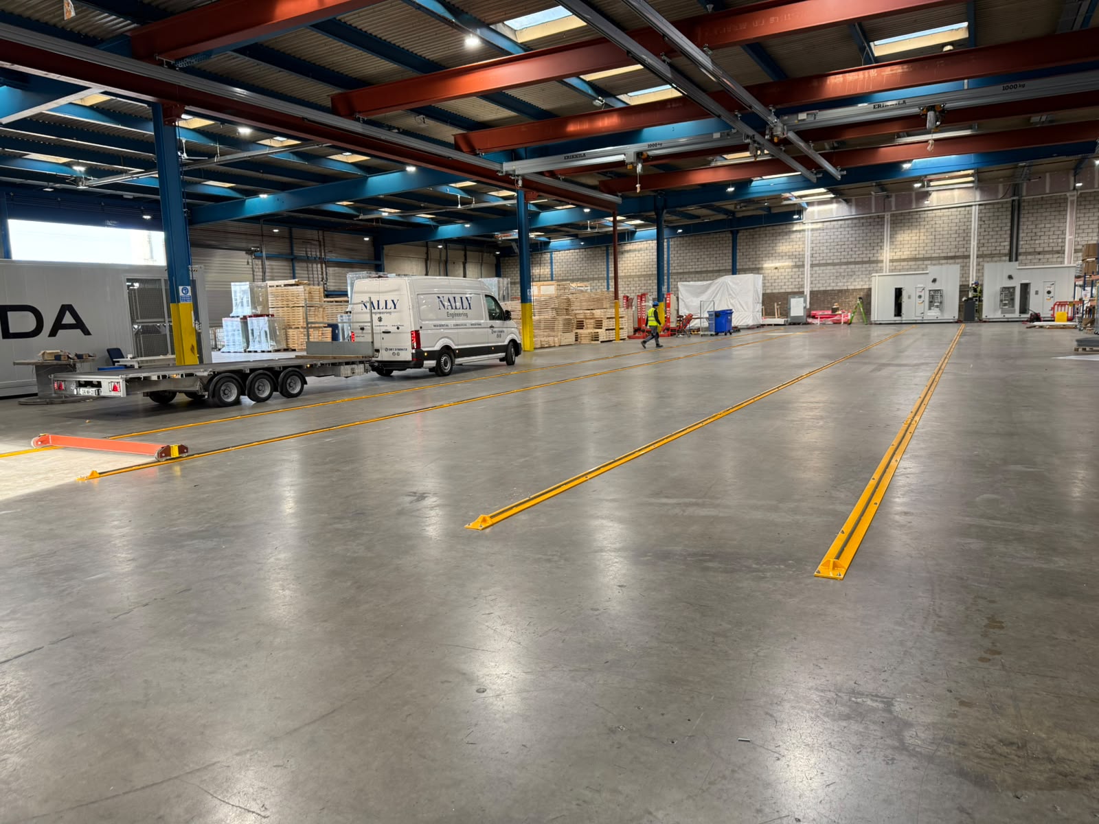 Wide view of yellow floor guide rails installed across a production hall with the Nally Engineering van alongside