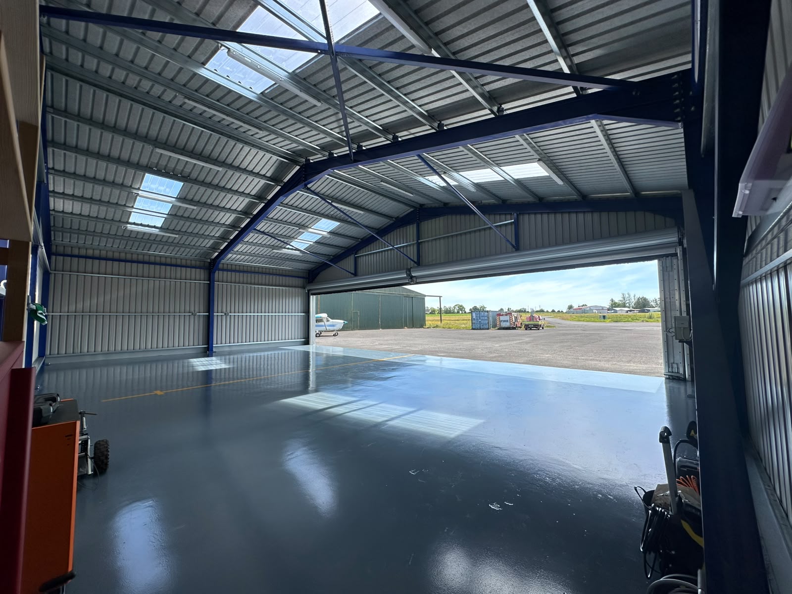 Inside the hangar looking out over the painted floor to the airfield, with blue portal frame and rooflights above