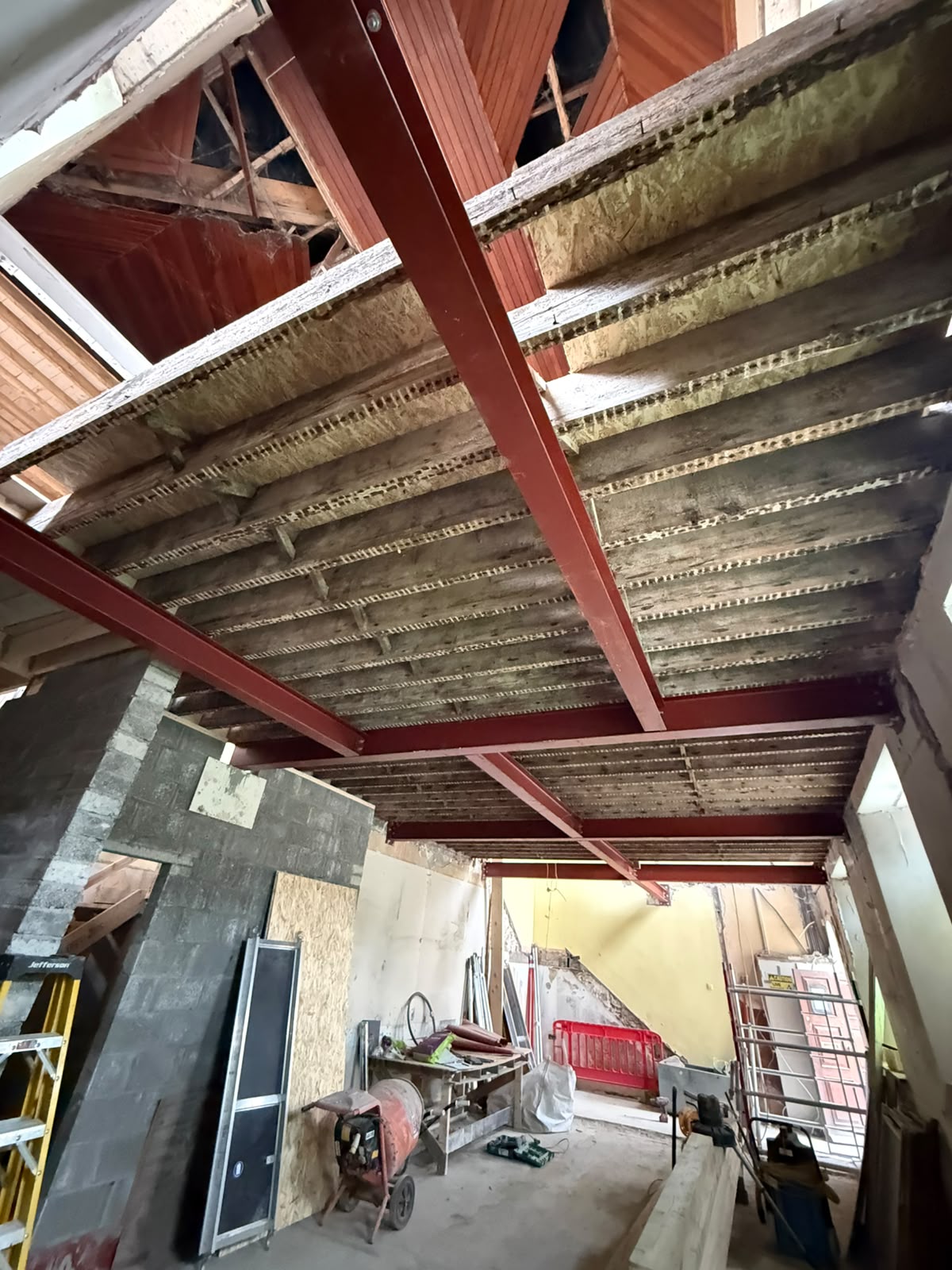 Red oxide steel beams carrying original timber joists and roof structure within an existing building
