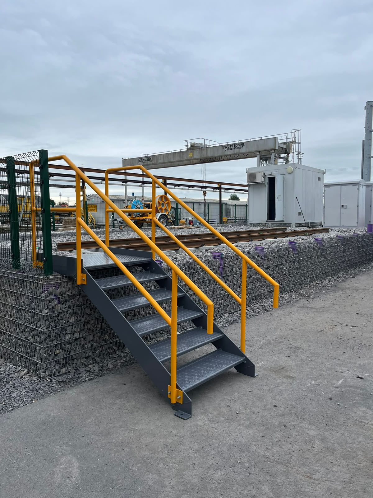Galvanised access stairs with yellow safety handrails serving a rail yard structure