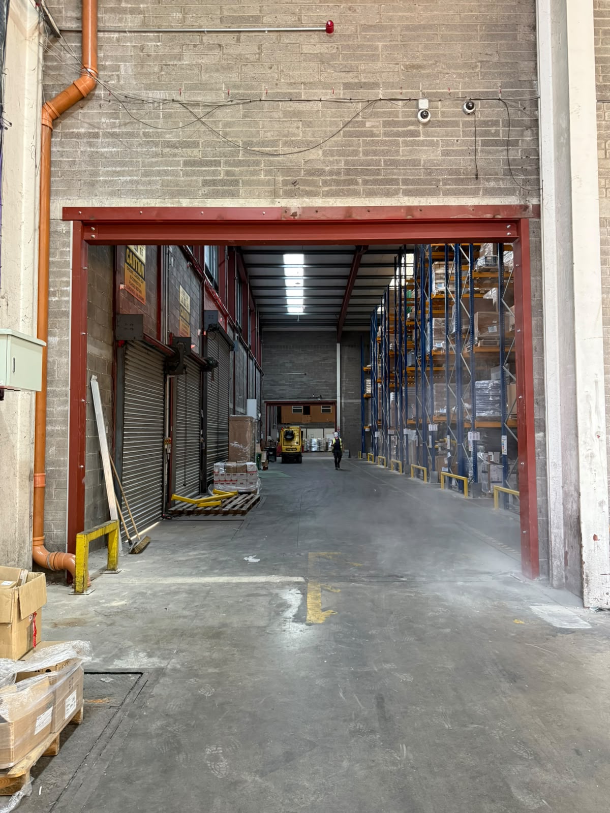 Red painted steel goal post frame forming a wide door opening between two warehouse bays