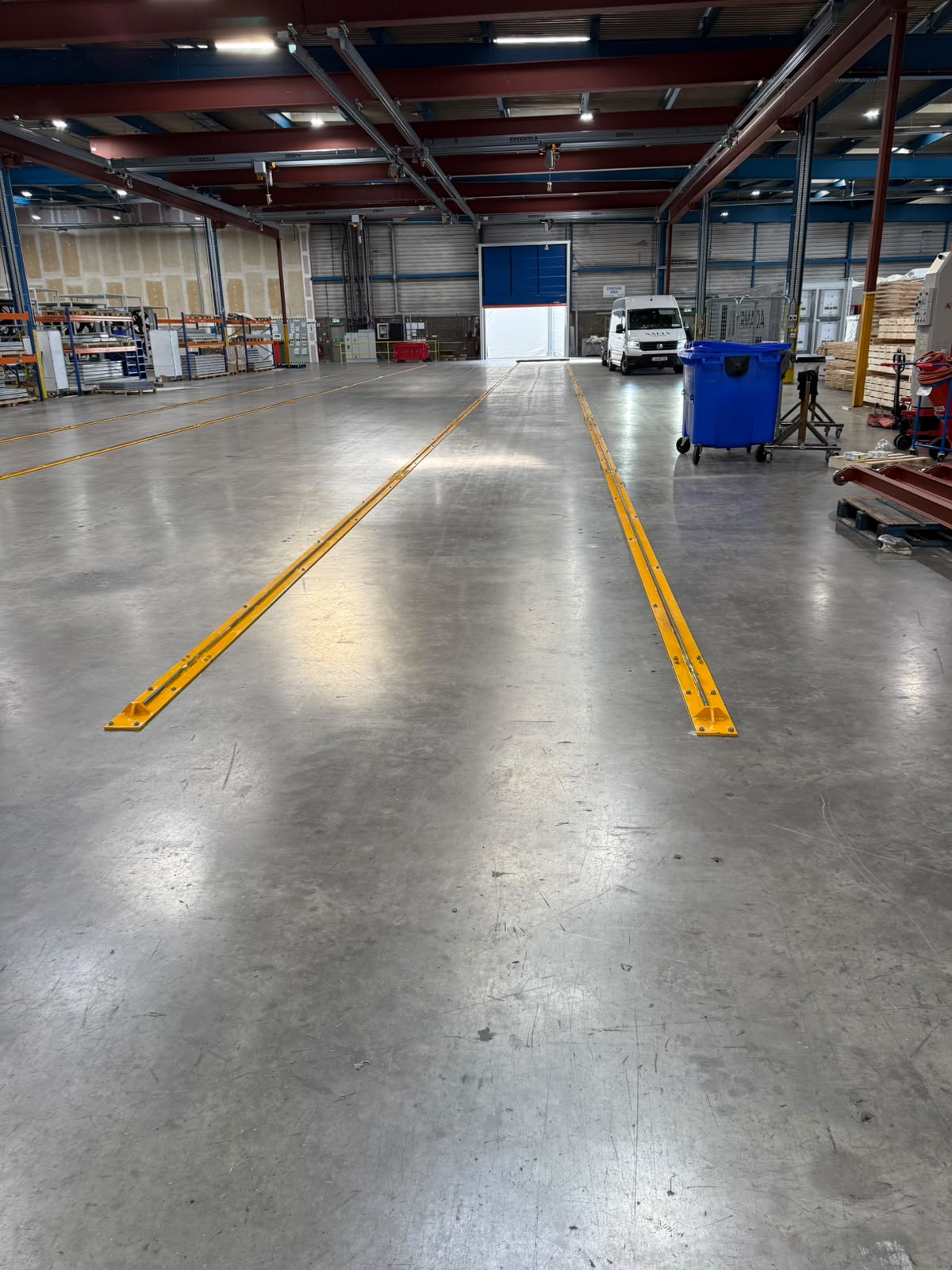 Parallel runs of yellow steel floor rail bolted into a polished concrete factory floor