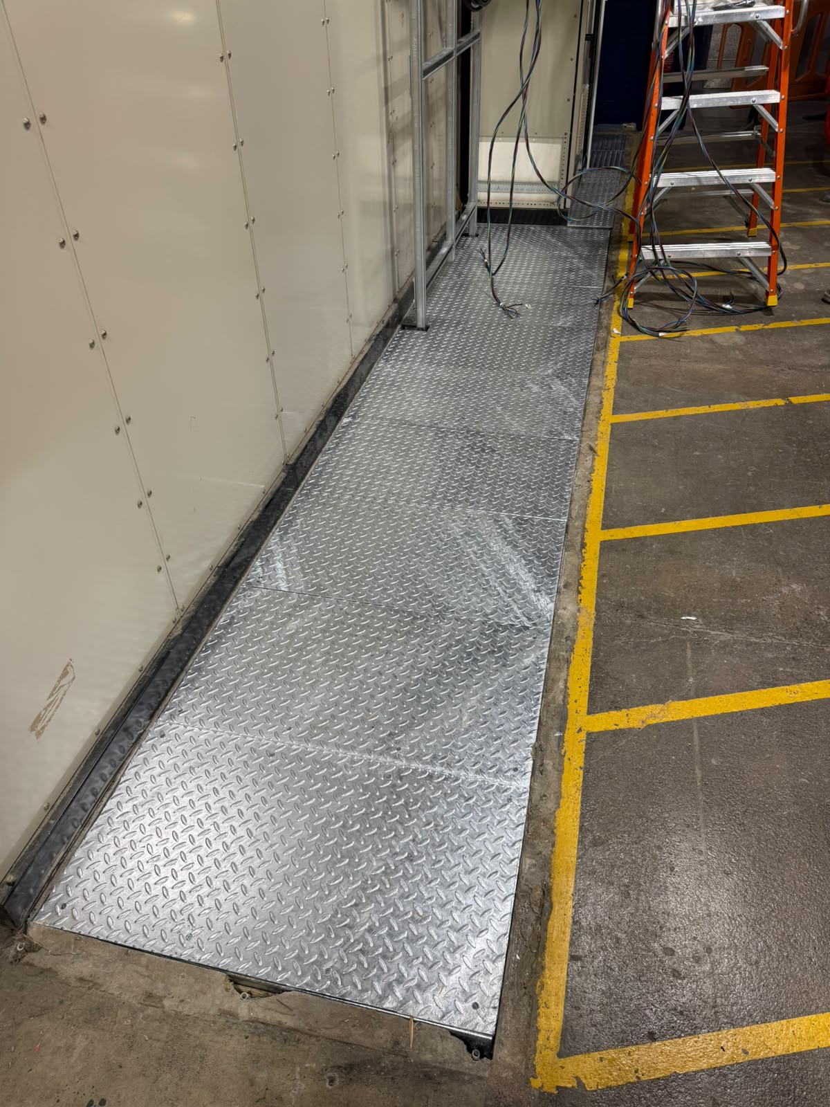 Long run of galvanised chequer plate covers set flush along a floor trench beside a control panel